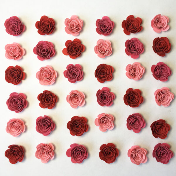 Gerollte Papierblumen in den Farben Rosa, Altrosa und Ziegelrot, angeordnet in Diagonalen